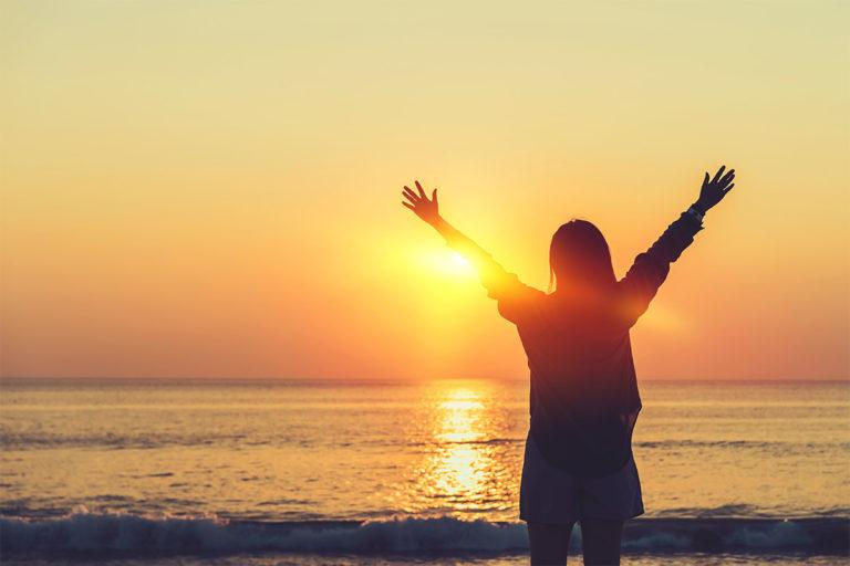 pensée-positive silhouette d'une femme qui lève les bras devant le couché de soleil