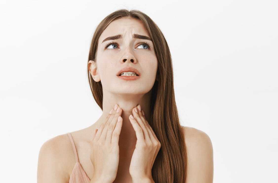 Angine blanche ou angine rouge ? femme brune qui se tient la gorge à 2 mains